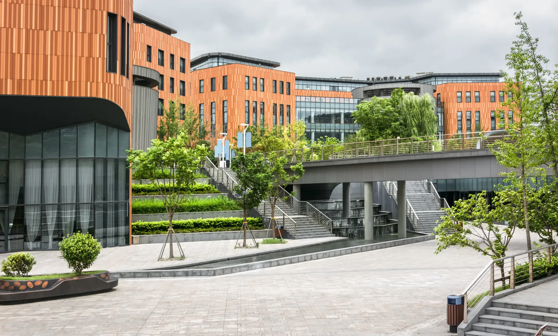 Moderne Architektur mit orangefarbenen Fassaden, Pflanzbeeten und Wegen in einem städtischen Außenbereich.