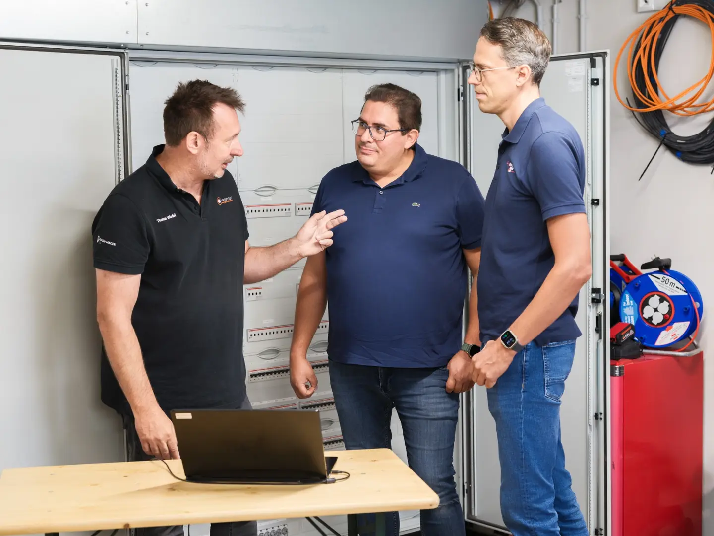 Drei Männer stehen um einen Laptop und diskutieren, während sie auf den Bildschirm schauen.
