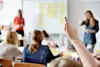 Ein Schüler hebt die Hand, um eine Frage im Unterricht zu stellen, während andere im Hintergrund aufmerksam sind.