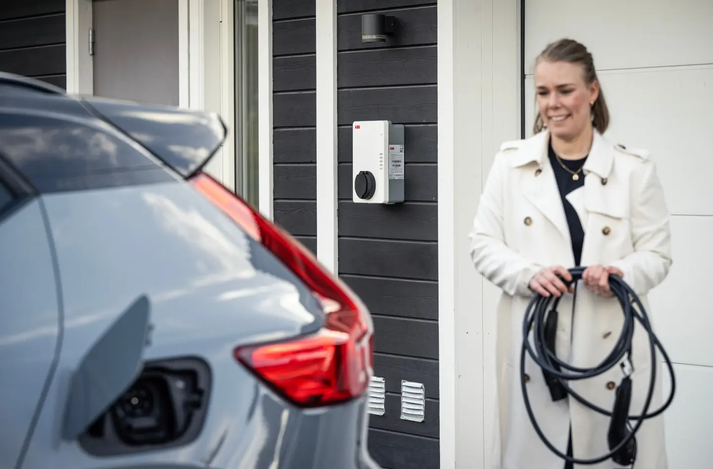 Eine Frau hält ein Ladekabel für ein Elektrofahrzeug, während sie vor einer Ladestation steht.