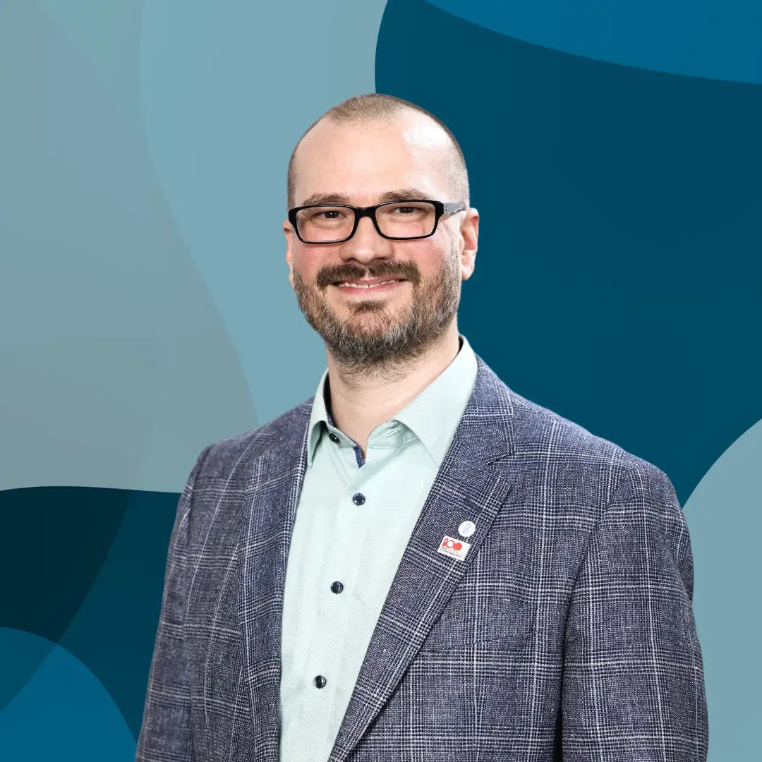 Porträt eines lächelnden Mannes mit Brille, einem karierten Jackett und einem hellen Hemd.