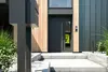 Moderne Haustür mit glatter Oberfläche und vertikaler Klinke, umgeben von Pflanzen und einem gepflasterten Weg.