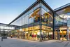 Modernes Einkaufszentrum mit großen Glasfassaden und sichtbaren Bekleidungsgeschäften im Erdgeschoss.