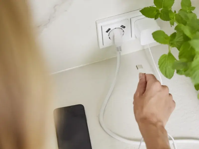 Een persoon steekt stekker in wandcontactdoos met randaarde
