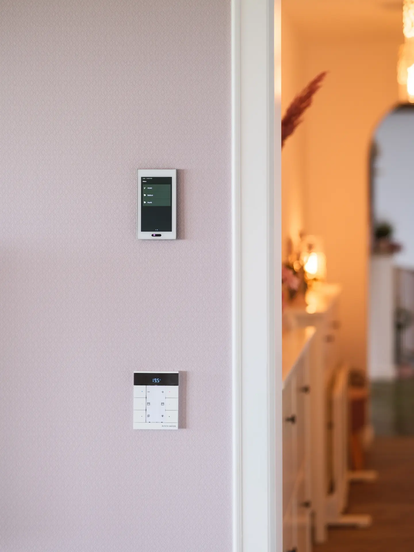 Zwei moderne Steuergeräte an einer Wand: ein Touchscreen oben und ein Bedienfeld mit Tasten darunter.