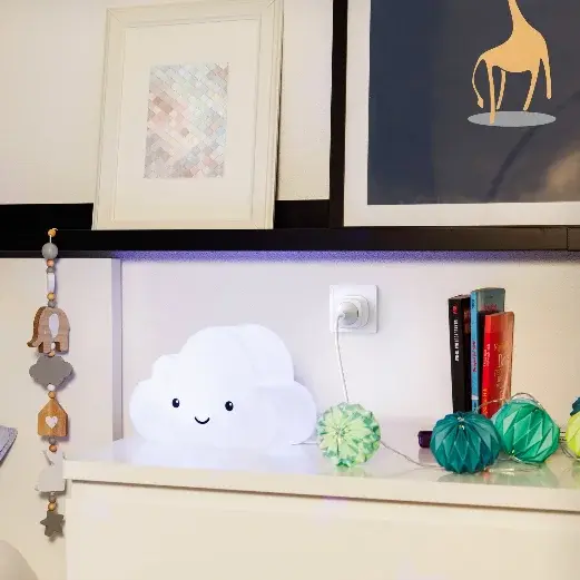 Een nachtkastje met een wolkenlamp, een boek, decoratieve elementen en een slaapkamer met een kussen.