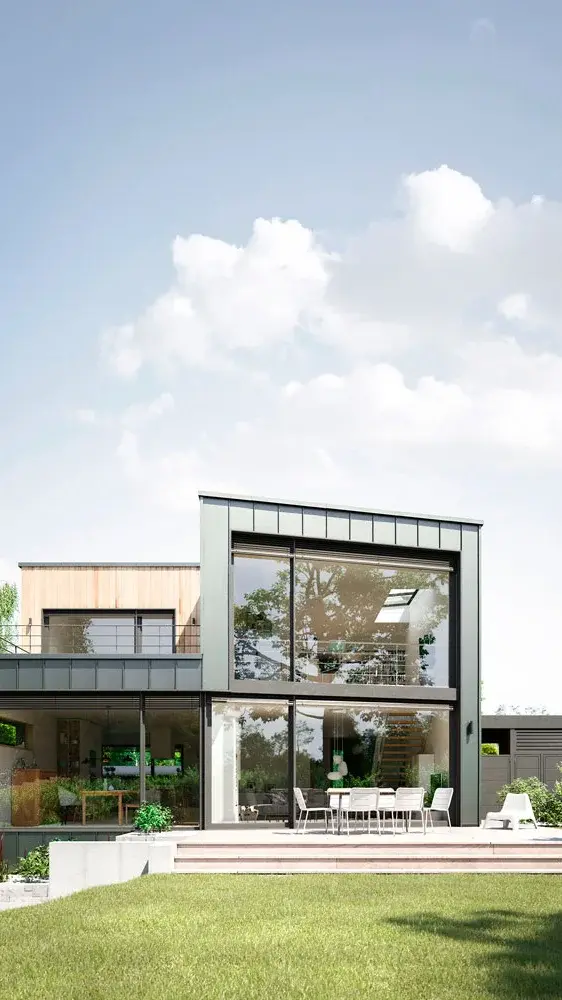 Moderne gevel van een woonhuis met twee verdiepingen, grote ramen en een terras, omgeven door gras en beplanting.