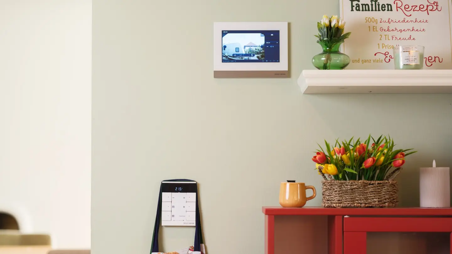 Ein Wanddisplay zeigt ein Bild, daneben ein Tisch mit einer Blumenvase, einer Tasse und einem Notizblock.