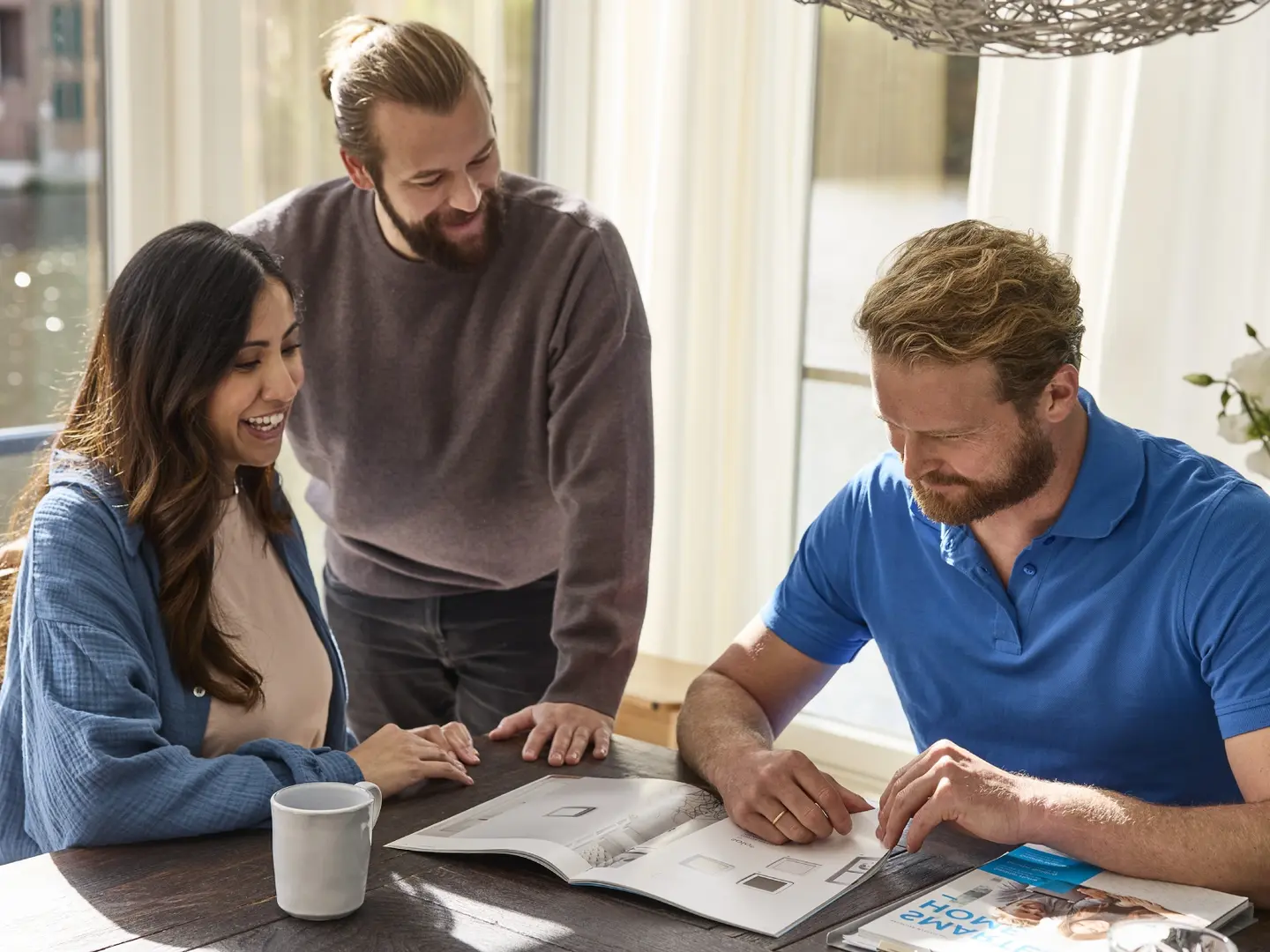 Drei Personen sitzen an einem Tisch und betrachten gemeinsam ein aufgeschlagenes Buch.