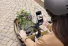 Frau mit Helm, die ein Smartphone in der Hand hält und ein Foto von sich selbst macht, während sie ein Lastenrad fährt.