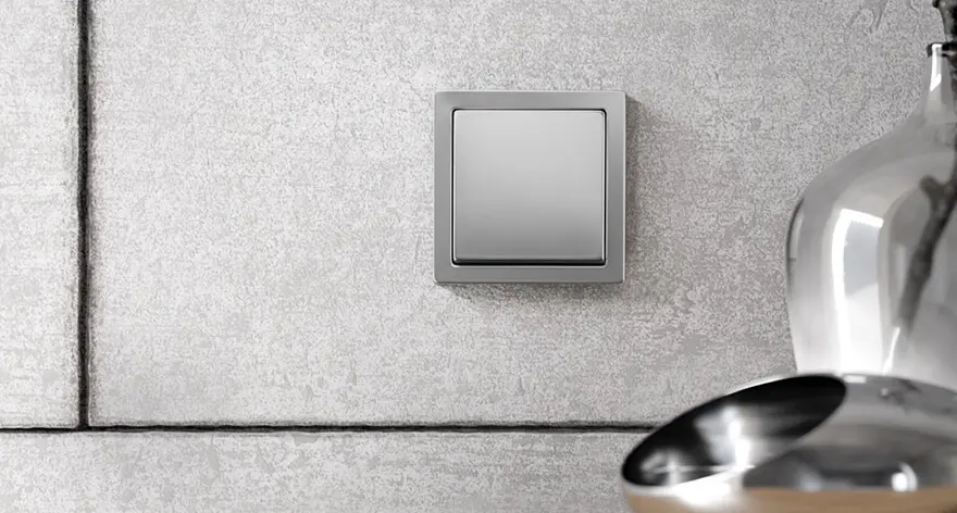 Moderner, quadratischer Lichtschalter in metallic-grauer Farbe an einer Wand.