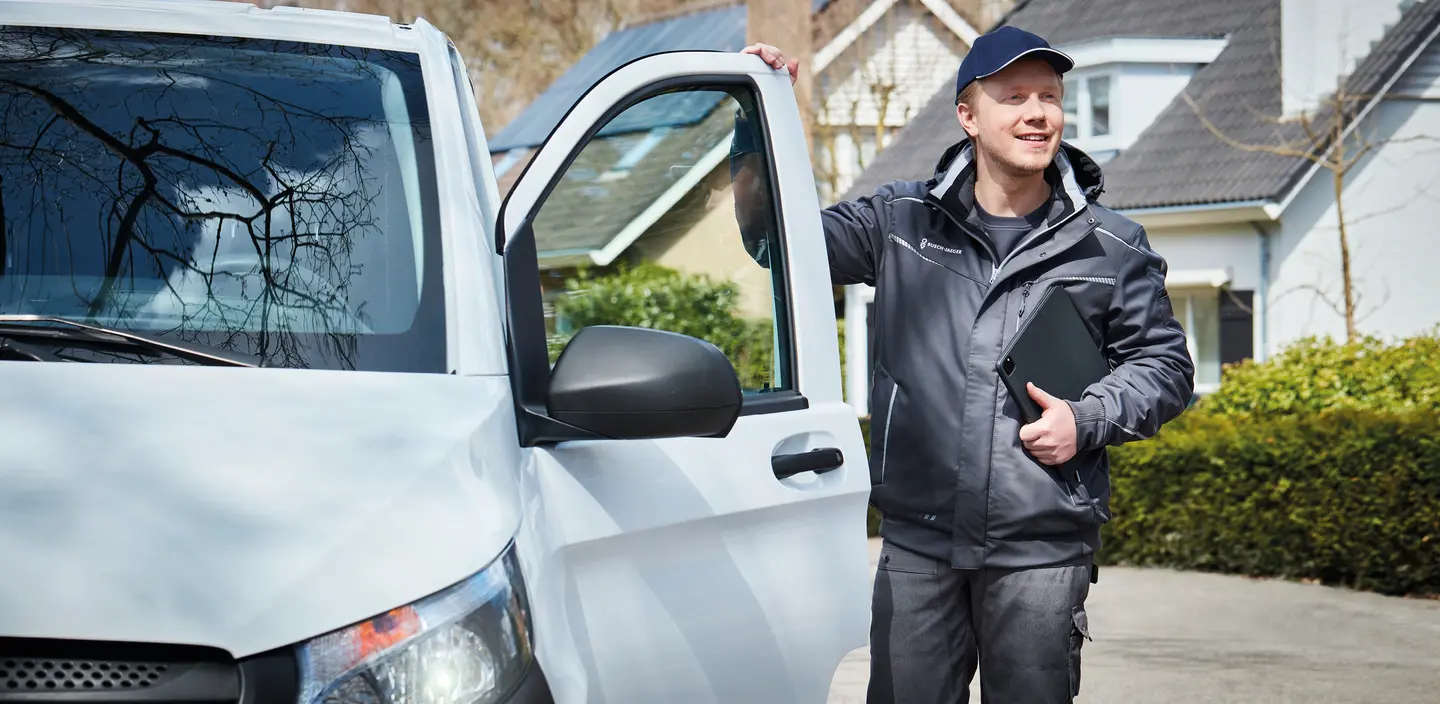 Ein Techniker in Arbeitskleidung, der an einem weißen Lieferwagen steht, hält einen Laptop in der Hand.