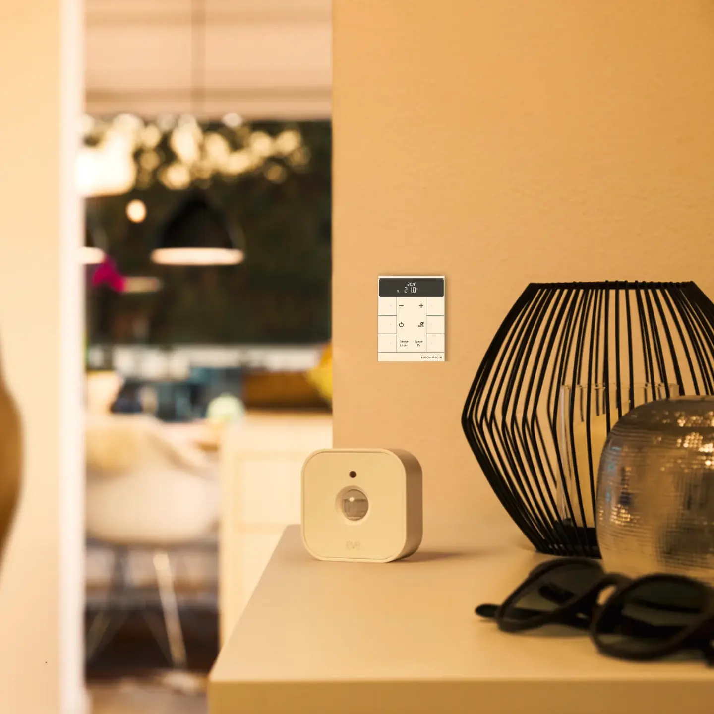 Een wit smart home-apparaat op een tafel, naast een moderne lamp en een zonnebril, terwijl iemand voorbijloopt. 